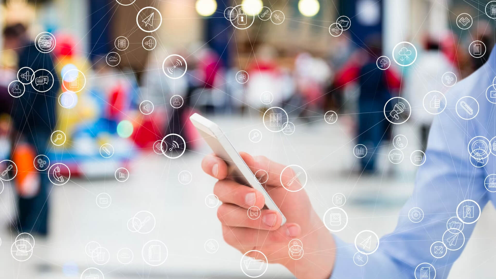 Hand holding a mobile phone with numerous icons around, symbolizing interactions.