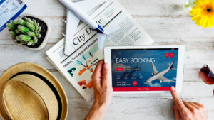Person holding an iPad with a travel booking image, surrounded by vacation-inspired elements